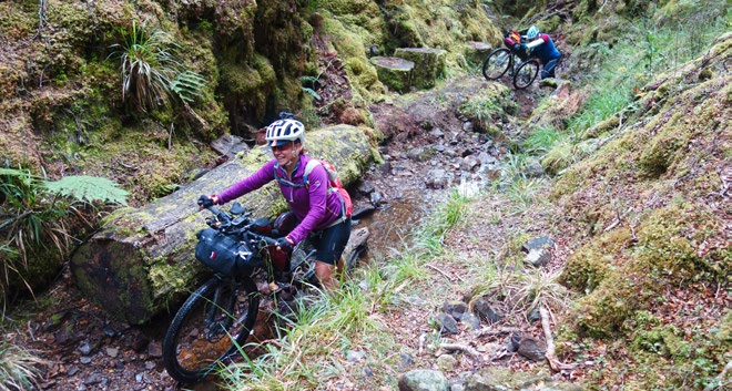 Cyclists push their bikes up a creek on the West Coast’s Waiuta Track